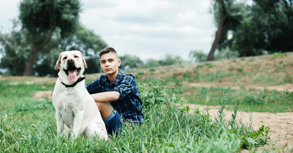 Un homme assis à côté de son chien dans l'herbe.